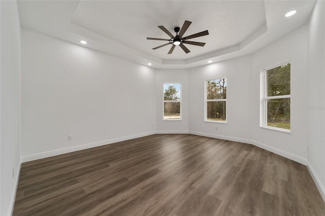 empty room with a raised ceiling, ceiling fan, and dark wood-type flooring