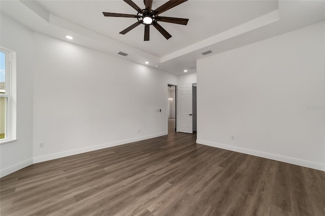 unfurnished room with a raised ceiling, ceiling fan, and dark wood-type flooring