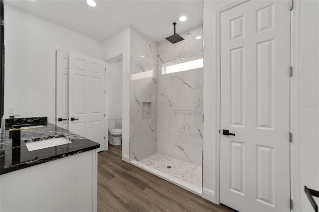 bathroom with hardwood / wood-style flooring, vanity, toilet, and tiled shower