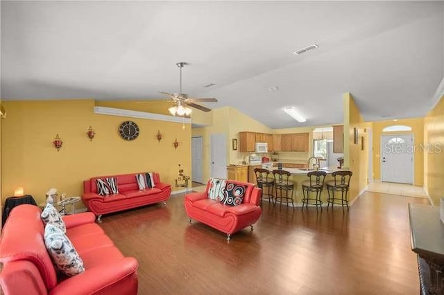 living room with ceiling fan, wood-type flooring, ornamental molding, and vaulted ceiling