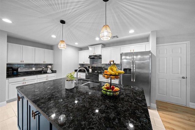 kitchen with white cabinets, stainless steel fridge with ice dispenser, sink, and an island with sink