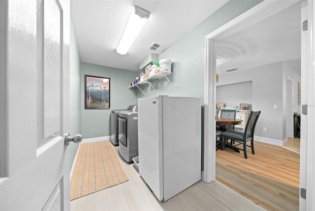 laundry room with washer and clothes dryer, light hardwood / wood-style floors, and a textured ceiling