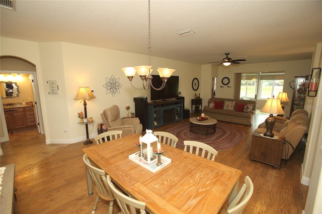 dining space with hardwood / wood-style floors, ceiling fan with notable chandelier, and a textured ceiling