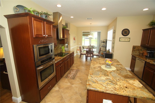 kitchen featuring wall chimney exhaust hood, light stone counters, backsplash, a kitchen island, and appliances with stainless steel finishes