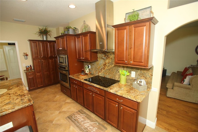 kitchen featuring light stone countertops, stainless steel appliances, wall chimney range hood, light hardwood / wood-style floors, and decorative backsplash