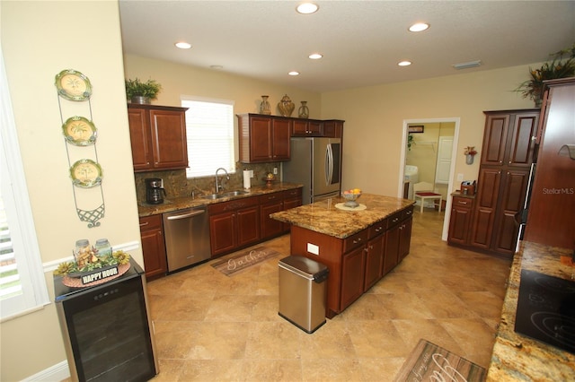 kitchen featuring backsplash, light stone counters, stainless steel appliances, sink, and a center island