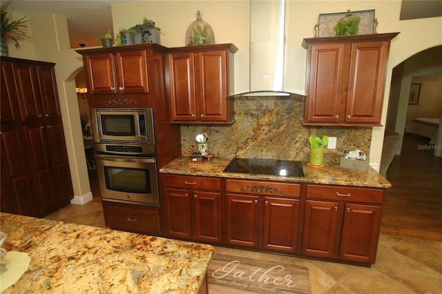 kitchen featuring light stone countertops, appliances with stainless steel finishes, tasteful backsplash, and wall chimney exhaust hood