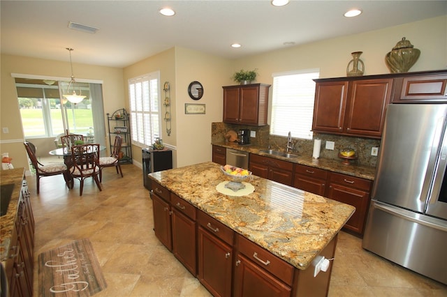 kitchen with sink, light stone counters, tasteful backsplash, a center island, and appliances with stainless steel finishes