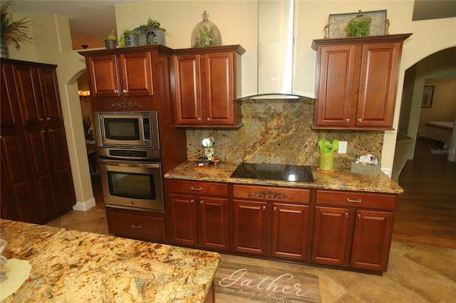 kitchen with wall chimney exhaust hood, appliances with stainless steel finishes, light stone counters, and backsplash