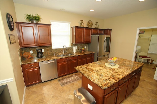 kitchen featuring sink, appliances with stainless steel finishes, a center island, tasteful backsplash, and light stone countertops