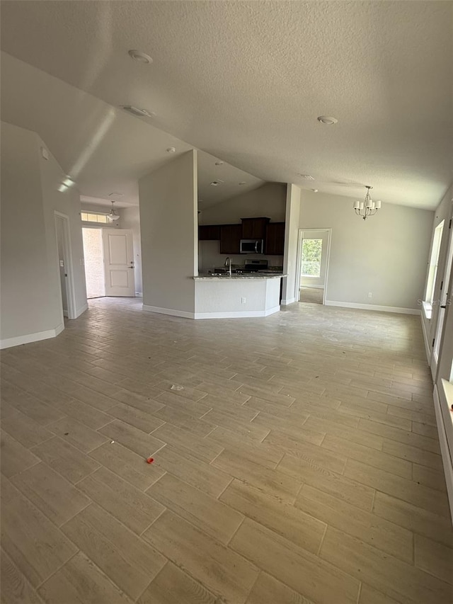 708 W Hallam Dr, Citrus Springs, FL 34434 - unfurnished living room featuring vaulted ceiling, light wood-type flooring, a chandelier, healthy amount of natural light, and a textured ceiling