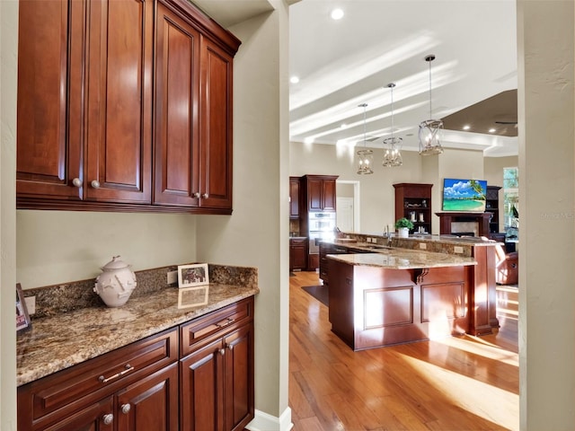 kitchen with a kitchen breakfast bar, light stone counters, decorative light fixtures, beamed ceiling, and light hardwood / wood-style floors