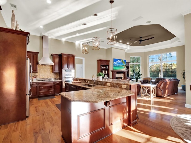 kitchen featuring wall chimney exhaust hood, sink, light hardwood / wood-style floors, hanging light fixtures, and a large island