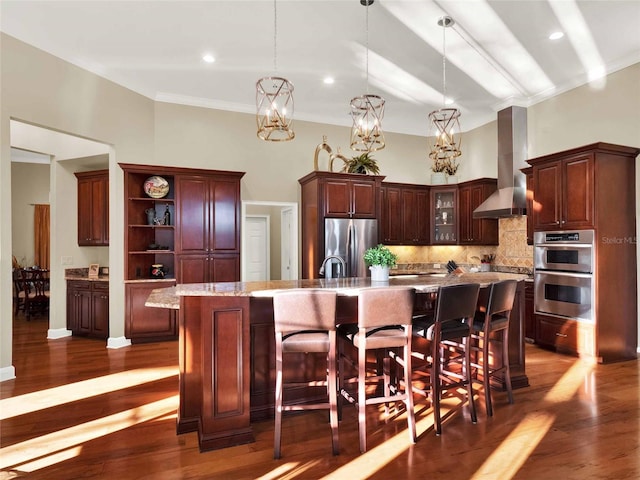 kitchen featuring a spacious island, pendant lighting, wall chimney exhaust hood, and stainless steel appliances