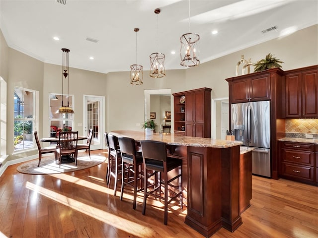 kitchen with stainless steel refrigerator with ice dispenser, light wood-type flooring, a large island, pendant lighting, and a breakfast bar area