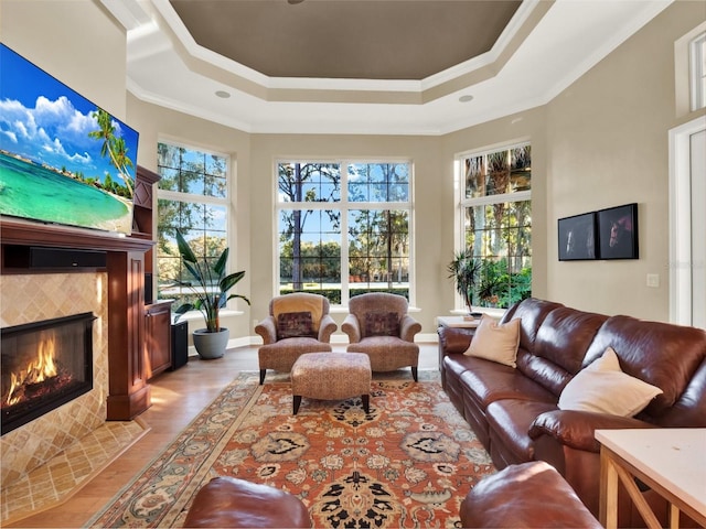 living room featuring a tray ceiling, a tiled fireplace, light hardwood / wood-style floors, and ornamental molding