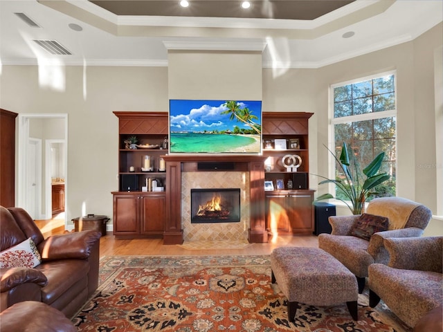 living room with a raised ceiling, crown molding, a fireplace, and light wood-type flooring