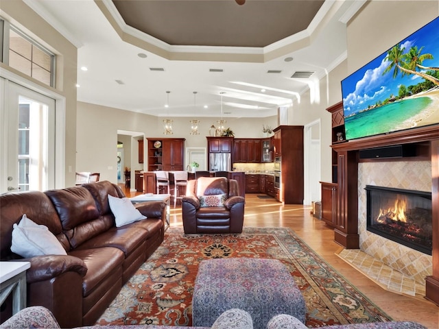 living room featuring a fireplace, a raised ceiling, light wood-type flooring, and crown molding