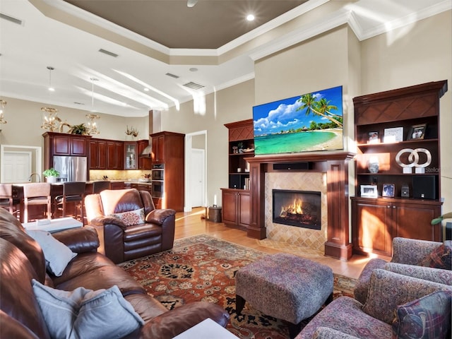 living room with a towering ceiling, ornamental molding, built in features, light hardwood / wood-style flooring, and a tiled fireplace