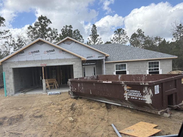 unfinished property with a garage, concrete block siding, and roof with shingles