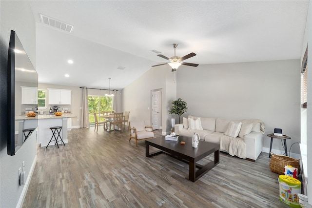 living room featuring ceiling fan with notable chandelier, dark wood-type flooring, and vaulted ceiling