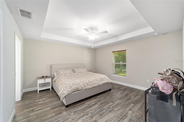 bedroom featuring a raised ceiling, ceiling fan, wood-type flooring, and a textured ceiling