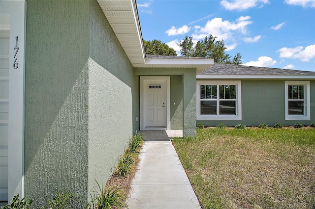 entrance to property featuring stucco siding and a yard