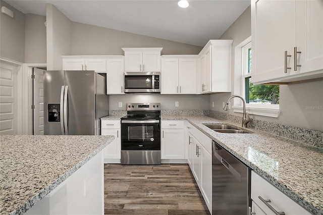 kitchen with a sink, dark wood-style flooring, stainless steel appliances, vaulted ceiling, and white cabinets