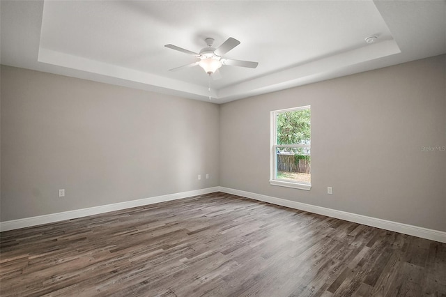 spare room with baseboards, a ceiling fan, dark wood-style flooring, and a tray ceiling