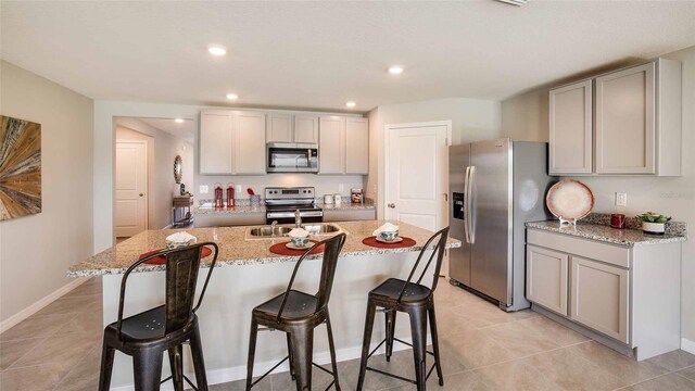 kitchen with gray cabinets, a breakfast bar, an island with sink, and appliances with stainless steel finishes