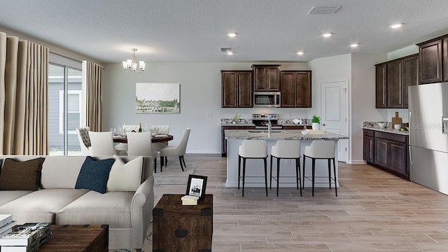 kitchen featuring light hardwood / wood-style flooring, stainless steel appliances, a textured ceiling, and an inviting chandelier