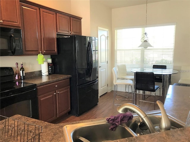 kitchen with sink, hardwood / wood-style flooring, hanging light fixtures, and black appliances