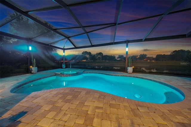 pool at dusk featuring glass enclosure, a patio area, and an in ground hot tub