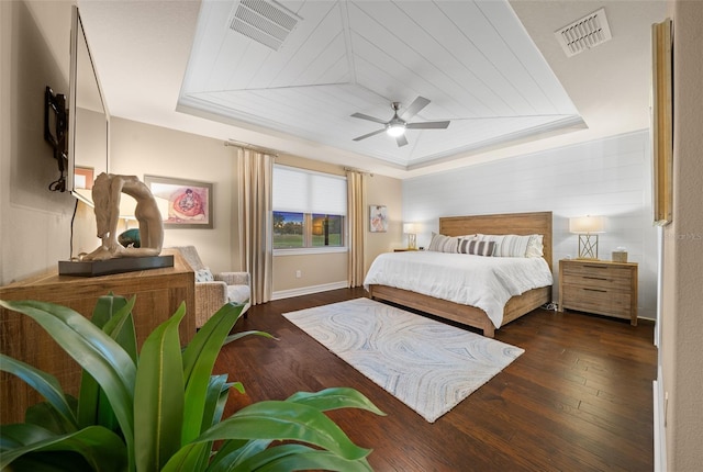 bedroom with ceiling fan, dark hardwood / wood-style floors, and a tray ceiling