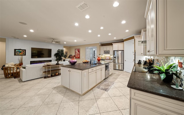 kitchen with a large island, ceiling fan, stainless steel appliances, crown molding, and dark stone counters