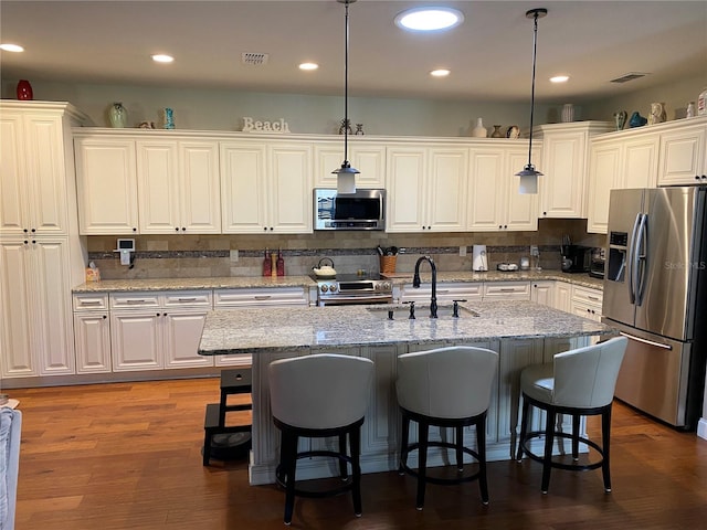 kitchen with stainless steel appliances, sink, pendant lighting, white cabinetry, and an island with sink