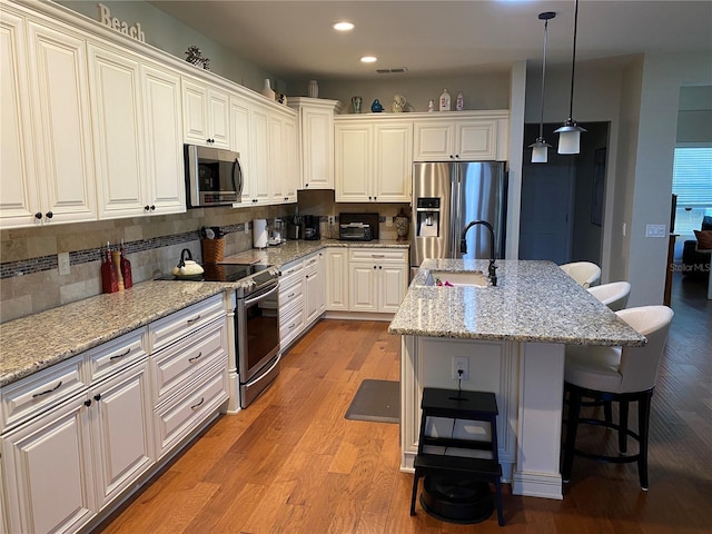 kitchen with a center island with sink, a kitchen breakfast bar, light wood-type flooring, appliances with stainless steel finishes, and white cabinetry