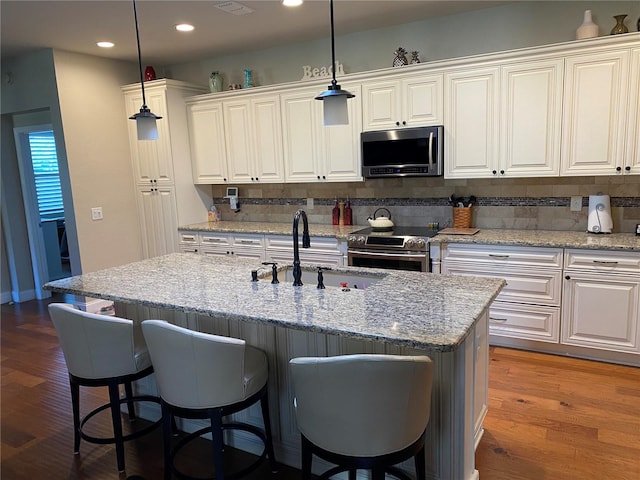 kitchen with a kitchen island with sink, stainless steel appliances, dark hardwood / wood-style floors, decorative backsplash, and white cabinets