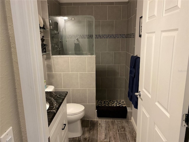 bathroom with vanity, tiled shower, wood-type flooring, tile walls, and toilet