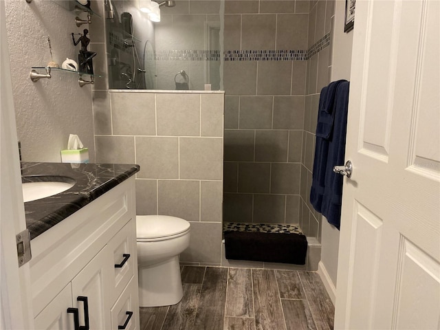 bathroom featuring vanity, toilet, a tile shower, and wood-type flooring