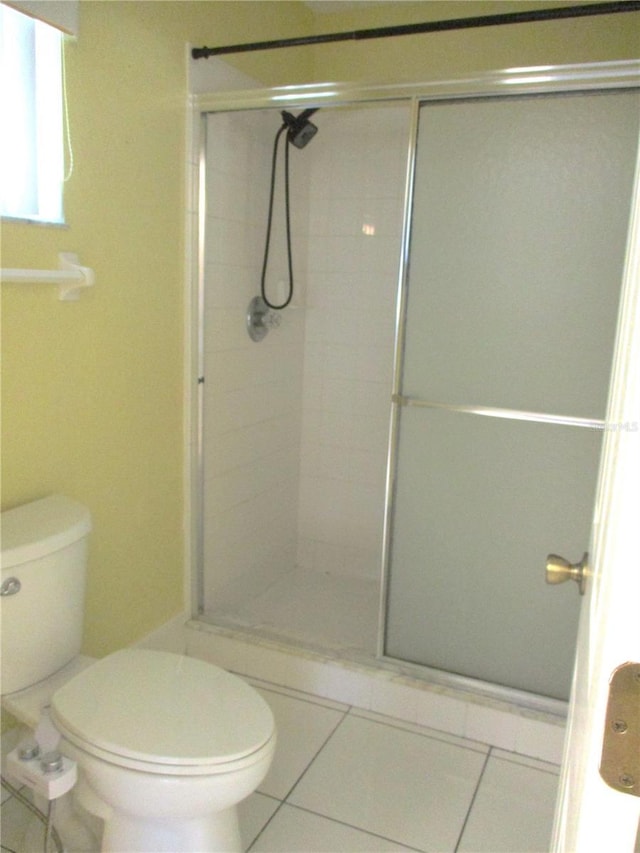 bathroom featuring tile patterned flooring, a shower with shower door, and toilet