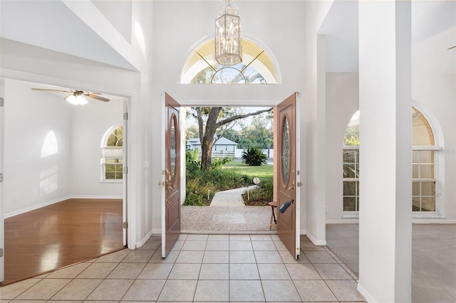 entryway with ceiling fan with notable chandelier, light carpet, and a high ceiling