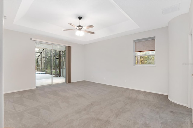 carpeted empty room with a tray ceiling, ceiling fan, and a healthy amount of sunlight