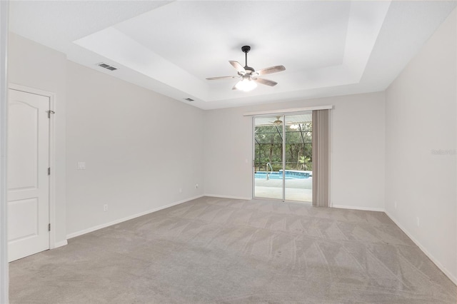 carpeted empty room featuring ceiling fan and a raised ceiling