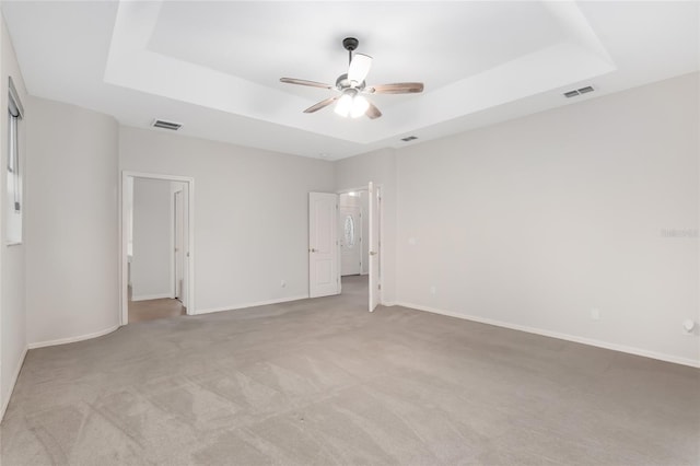 unfurnished bedroom featuring light colored carpet, a raised ceiling, and ceiling fan