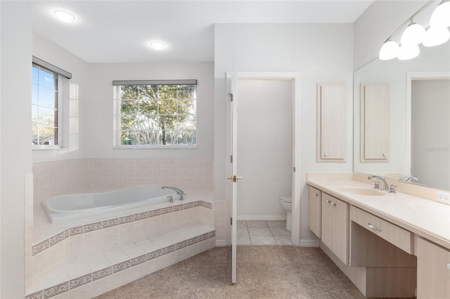 bathroom featuring tile patterned flooring, vanity, tiled bath, and toilet