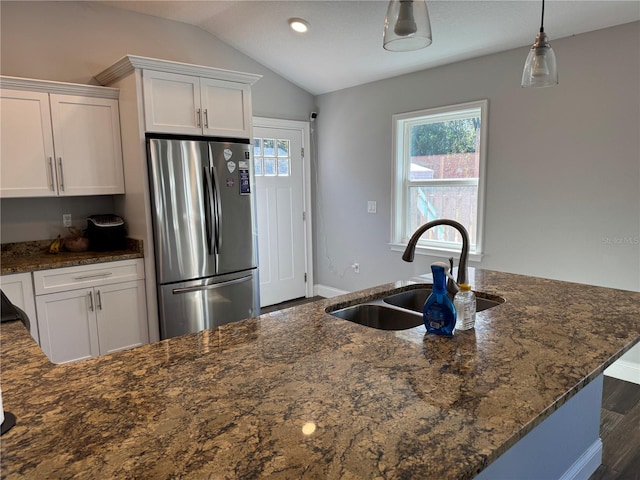 kitchen with dark stone counters, vaulted ceiling, sink, white cabinetry, and stainless steel refrigerator