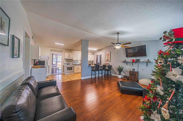 living room with ceiling fan, light hardwood / wood-style floors, a textured ceiling, and vaulted ceiling