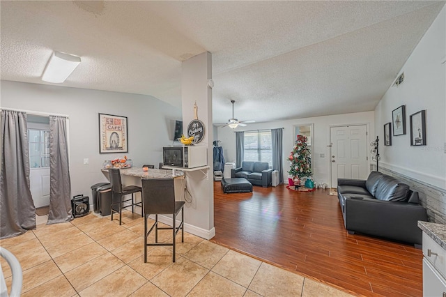 living room with ceiling fan, light wood-type flooring, a textured ceiling, and vaulted ceiling