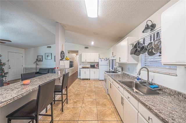 kitchen featuring sink, vaulted ceiling, a textured ceiling, white appliances, and white cabinets